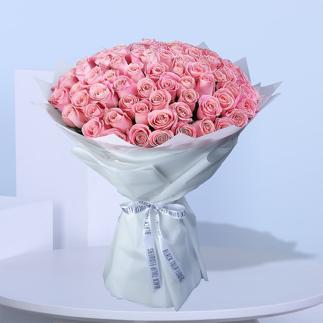 A large bouquet of light pink roses wrapped in white paper with white ribbons.
