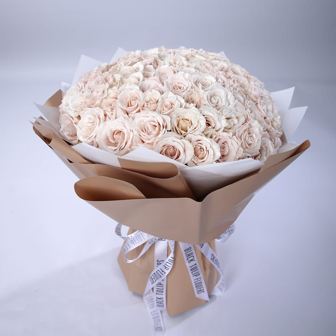 Luxurious bouquet of 100 creamy white roses wrapped in brown paper tied with white ribbon.