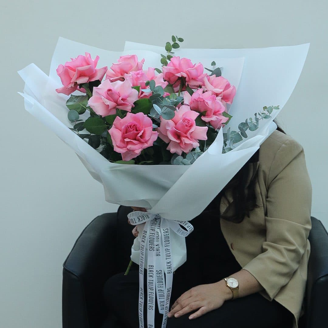 Bouquet featuring 10 delicate pink roses paired with eucalyptus, wrapped in a white covering and tied with a white ribbon.