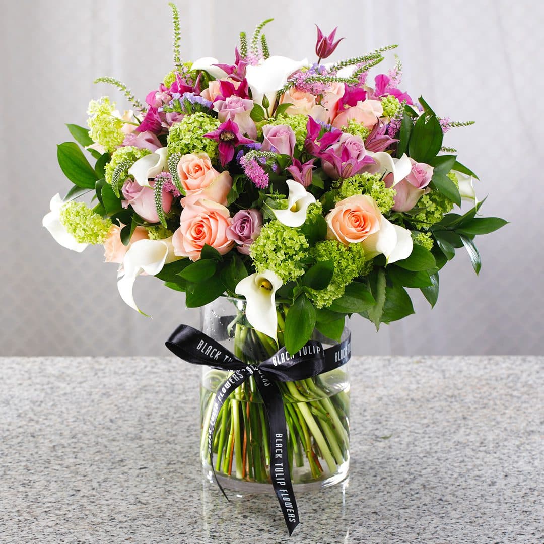Mix of fresh, vibrant flowers arranged in a clear glass vase tied with a black ribbon.