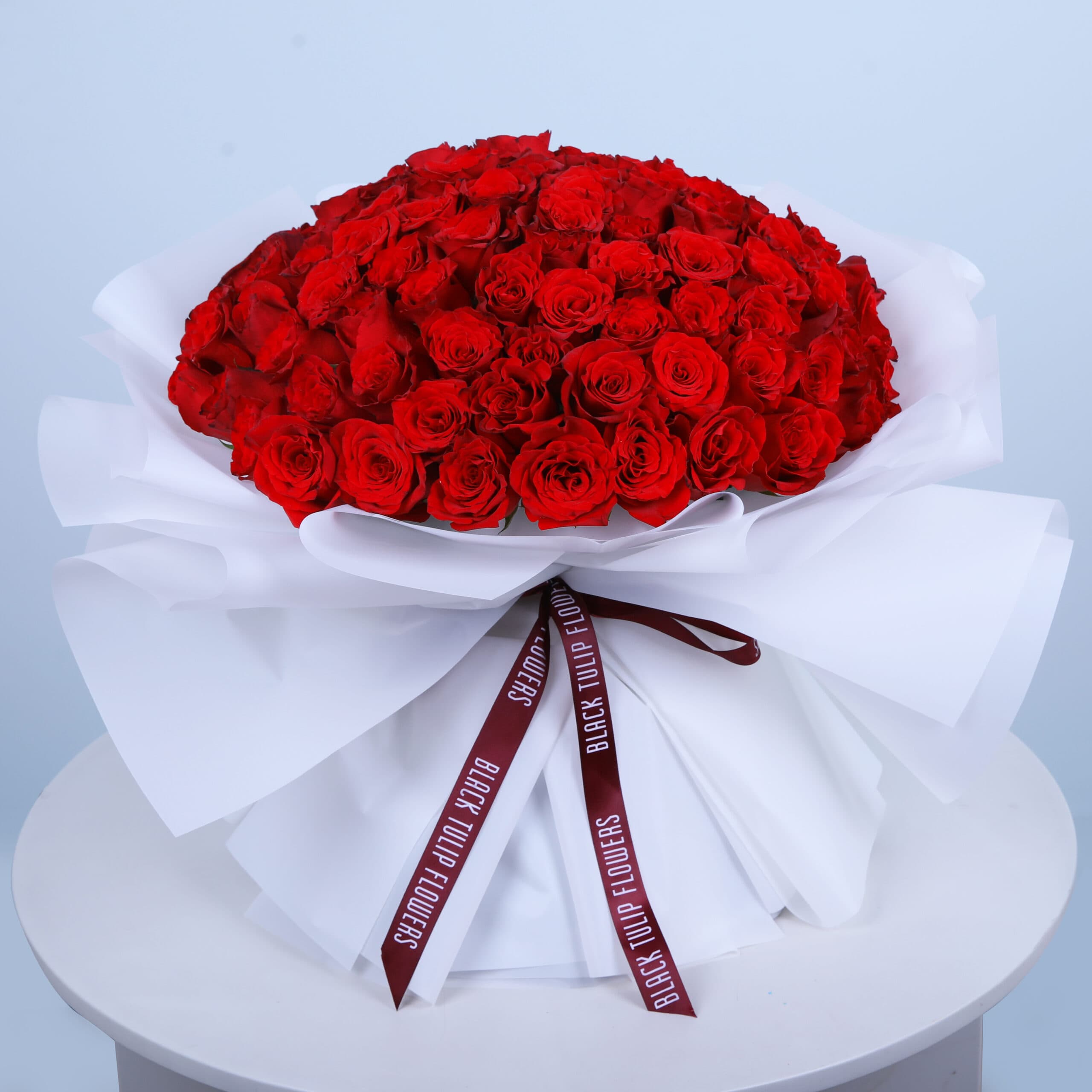 Bouquet of 101 red roses tied elegantly arranged in white wrap and tied with maroon ribbon.