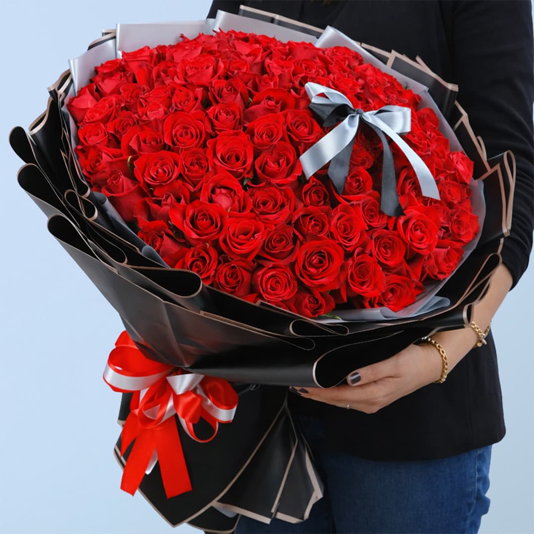 A woman with a stunning bouquet of 100 red roses, highlighting the flowers' vivid color and abundant petals.