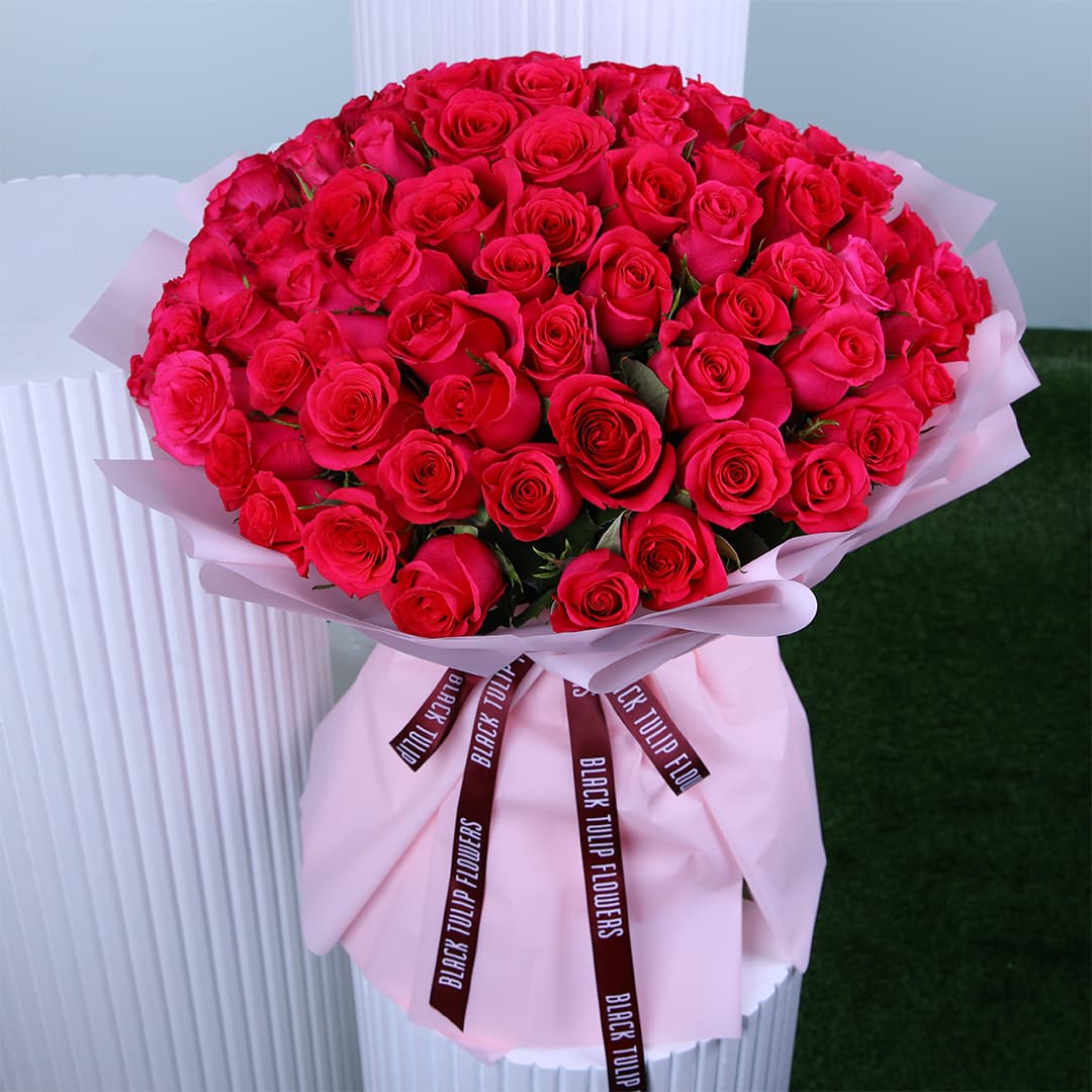 A rounded bouquet of Dark pink roses wrapped in pink paper with a "BLACK TULIP FLOWERS" ribbon, against a white and green background