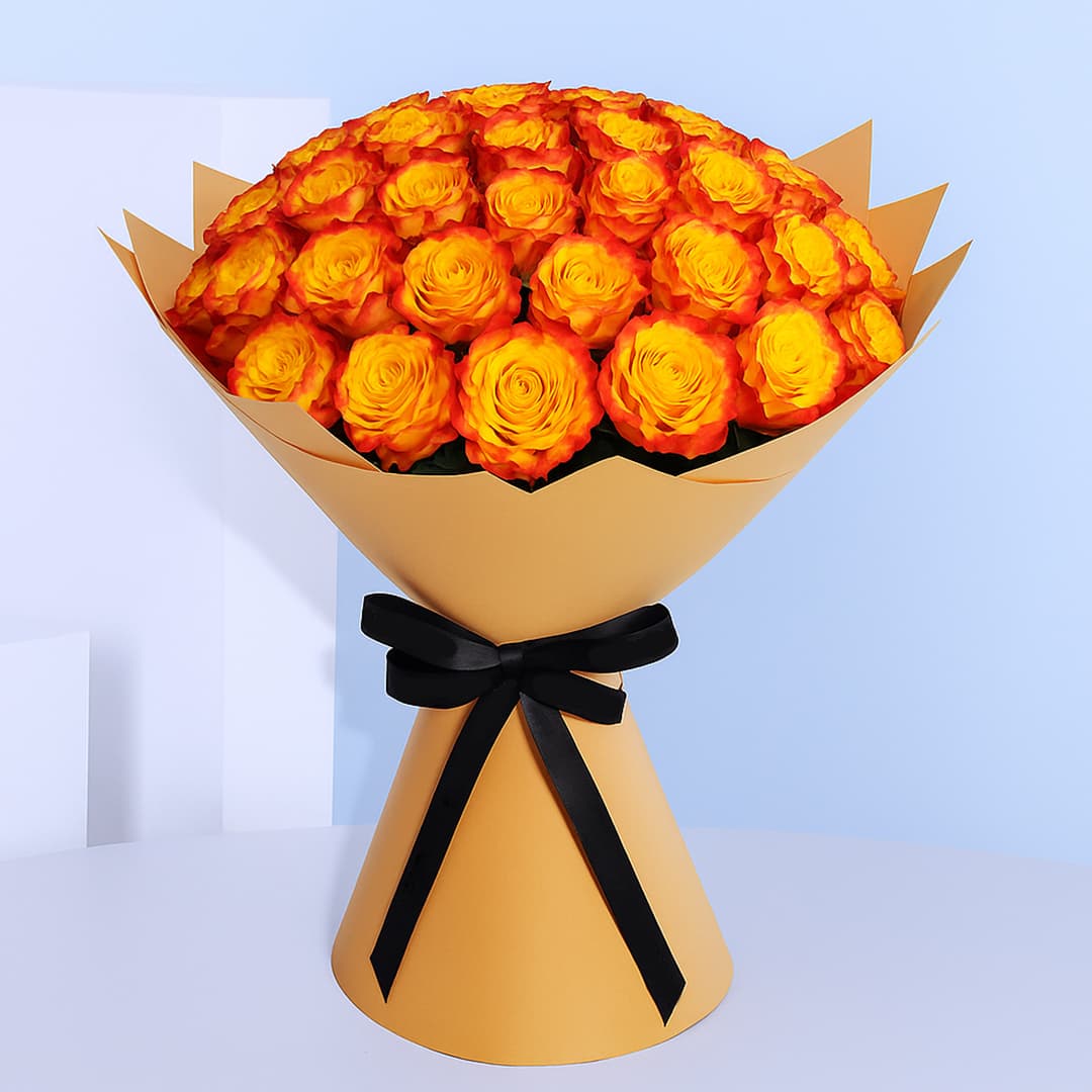 A large bouquet composed of numerous roses with bright yellow centers and vivid orange edges, wrapped in light brown paper and tied with a black ribbon.