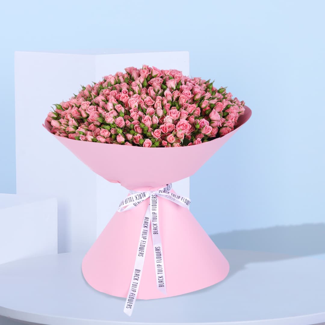 A large bouquet of 100 pink spray roses wrapped in pink paper with a white ribbon.