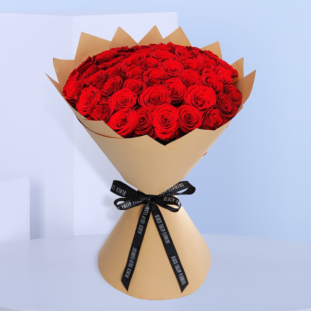 A premium bouquet of red roses elegantly wrapped in brown paper and tied with a black ribbon.