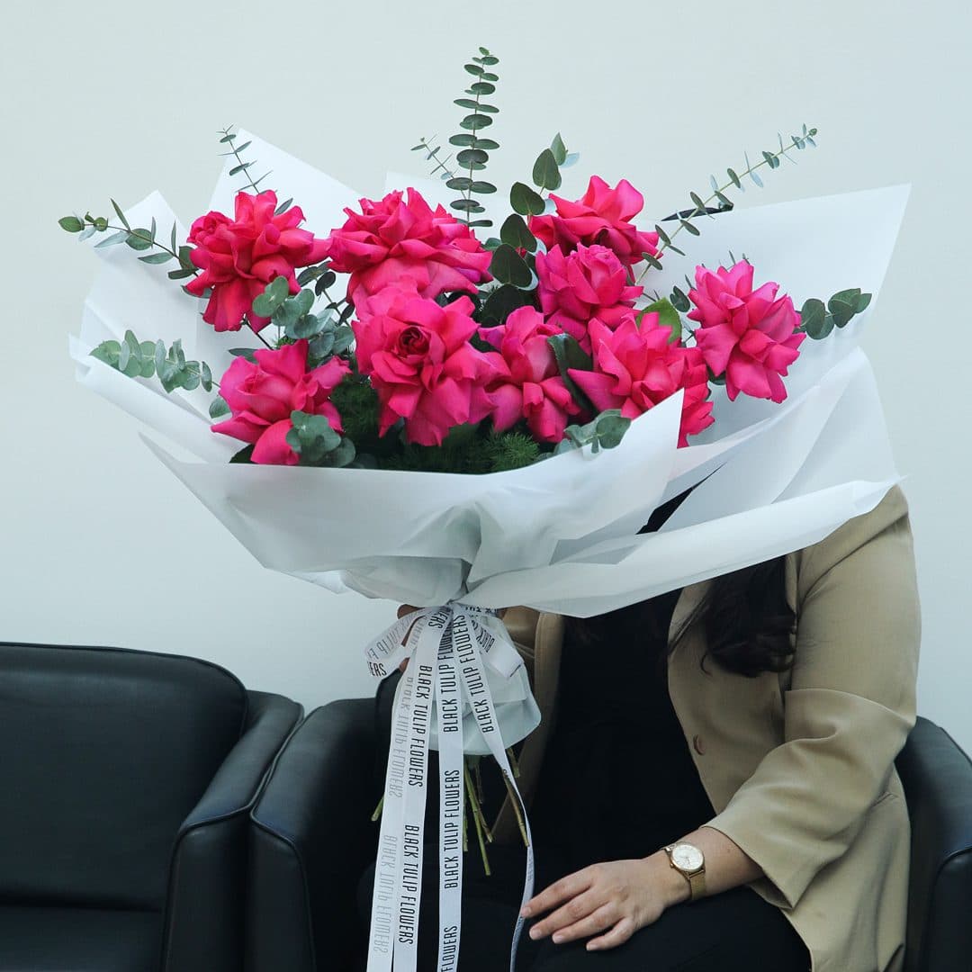 Pink rose bouquet with eucalyptus in white wrap, tied with white ribbon.