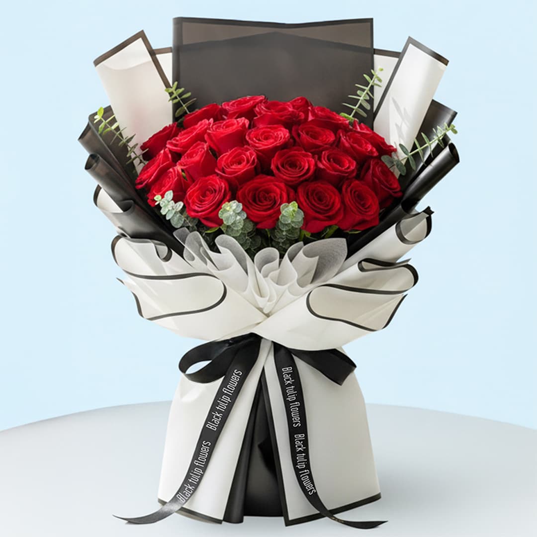 A hand-tied bouquet of vibrant red roses arranged with green eucalyptus stems and wrapped in stylish black and white secured with a black ribbon.