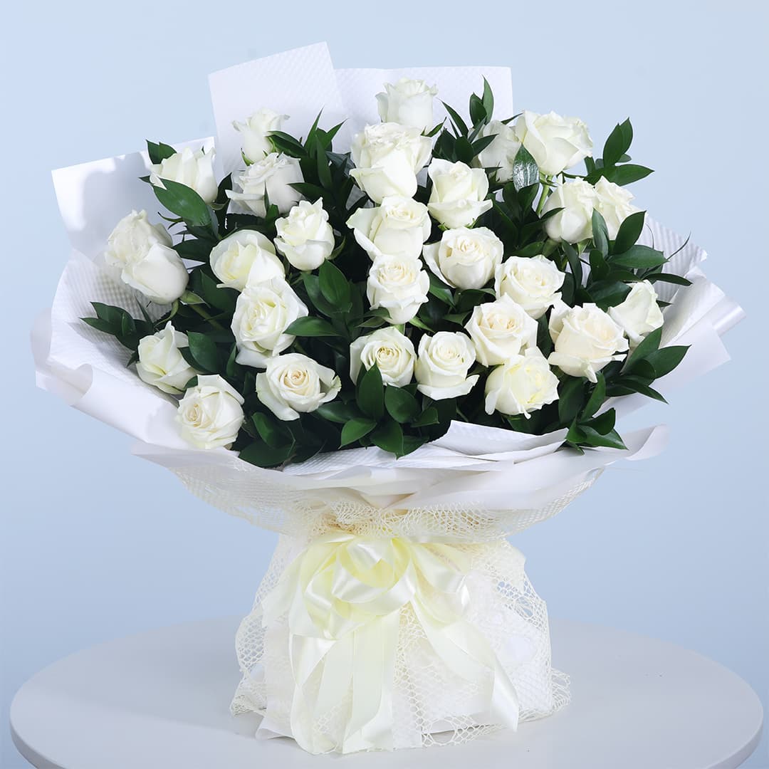 Bouquet of 30 white roses with fresh green leaves in a white wrap and tied with a white ribbon.