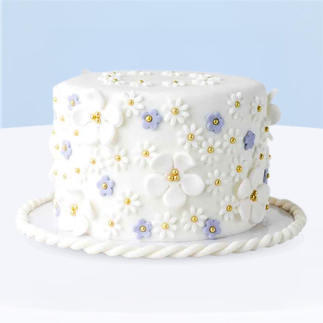 White flower-themed fondant cake decorated with pastel lilac flowers and gold pearls.