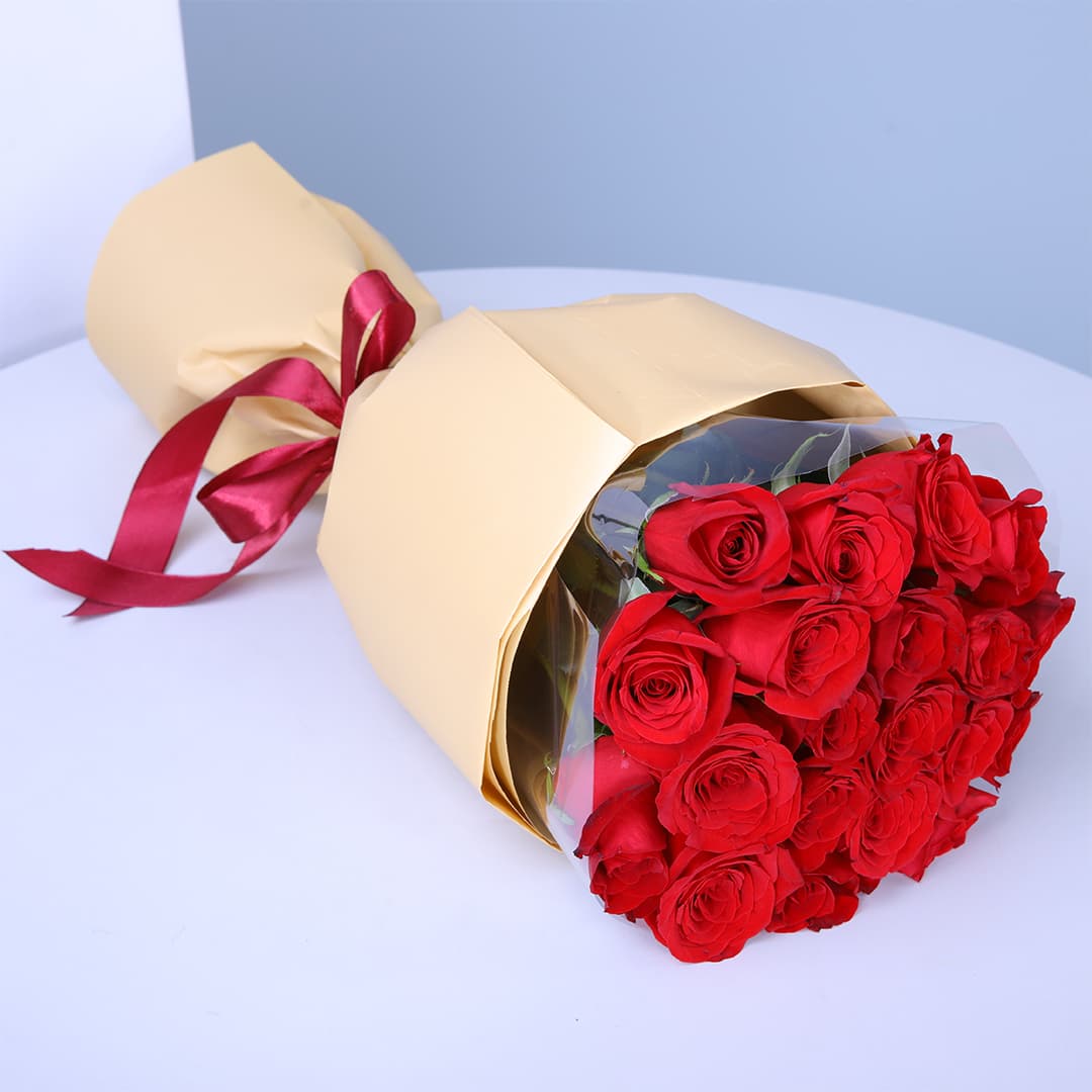 20 vibrant red roses wrapped in soft peach paper and finished with a maroon ribbon.