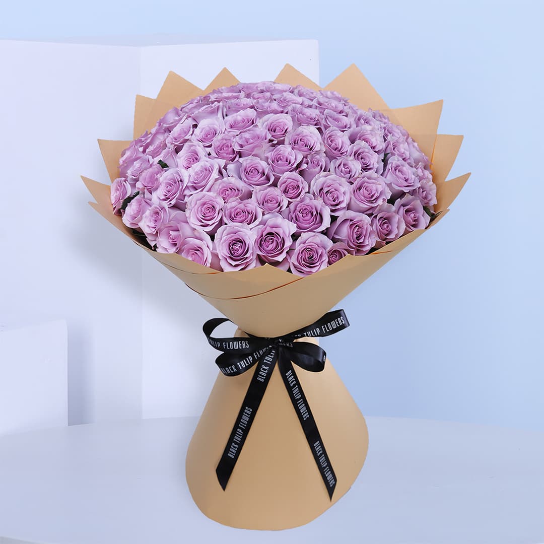 A bouquet of Purple roses wrapped in kraft paper tied with black ribbon.