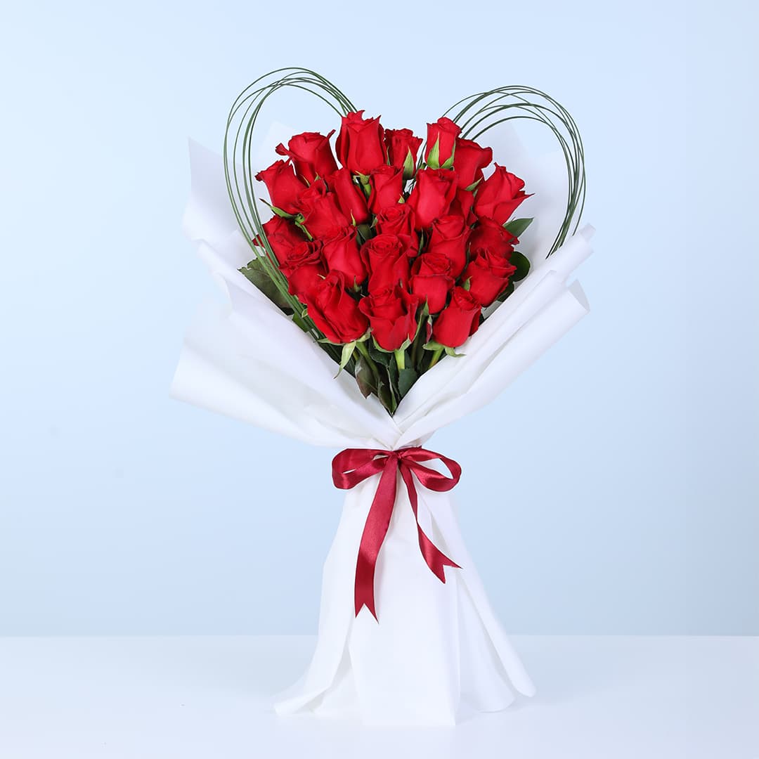 20 red roses arranged in a heart-inspired outline with loop accents in white wrapping, finished with a red ribbon.