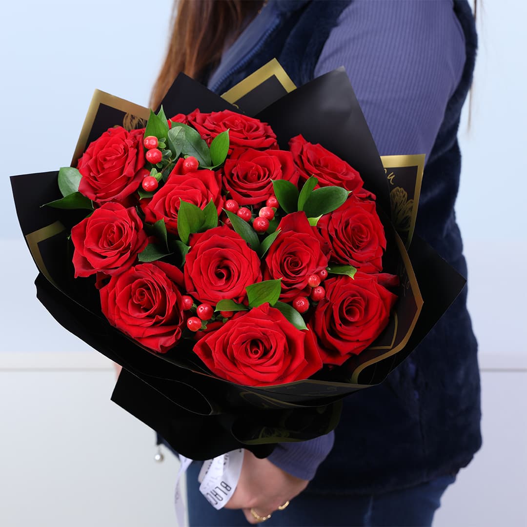 12 red roses bouquet with ruscus greenery and red hypericum in a designer wrap For Love.