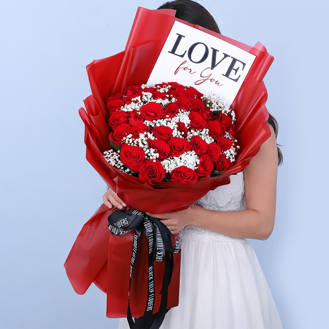Hand-tied Valentine bouquet featuring 25 fresh red roses and 5 white gypso fillers wrapped in a red sheet and secured with a black ribbon