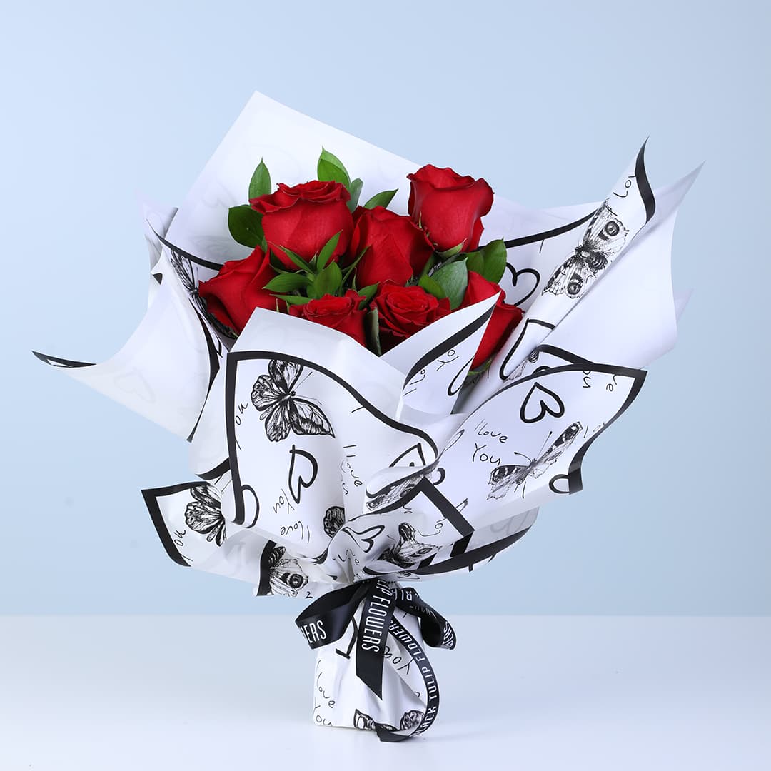 Red roses with fresh green leaves in a black-and-white printed wrap