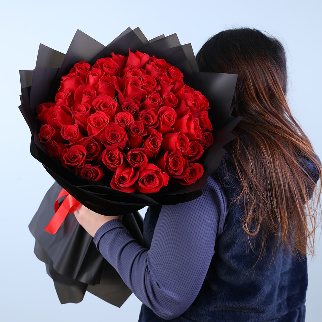 Bouquet featuring premium red roses in layered black wrapping with a red satin ribbon.