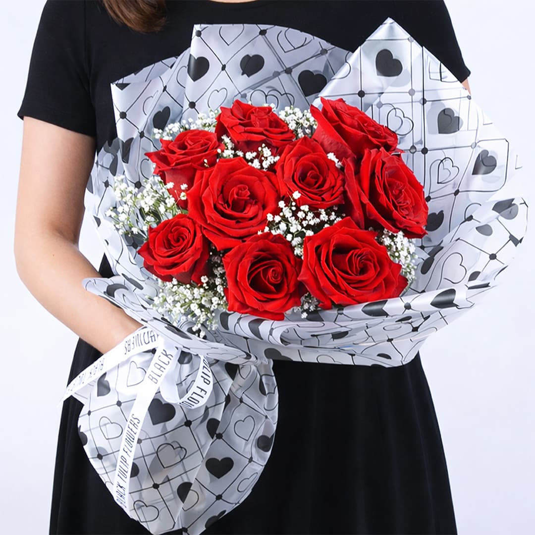 A bouquet of red roses and baby’s breath in a heart-patterned white wrap, finished with a Valentine’s Day romantic presentation.