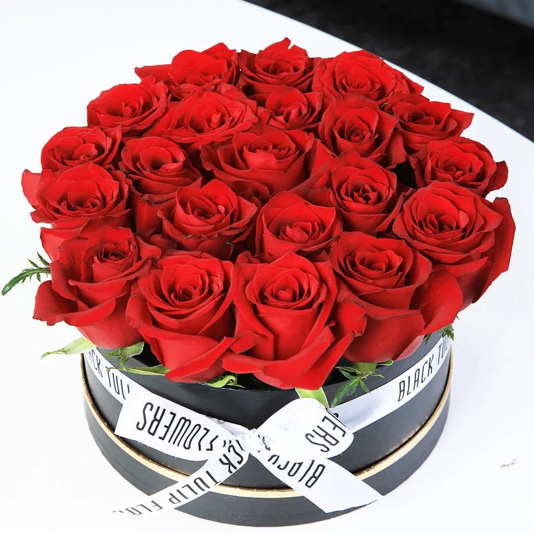 Stunning display of red roses arranged in a black box, elegantly tied with a white ribbon.