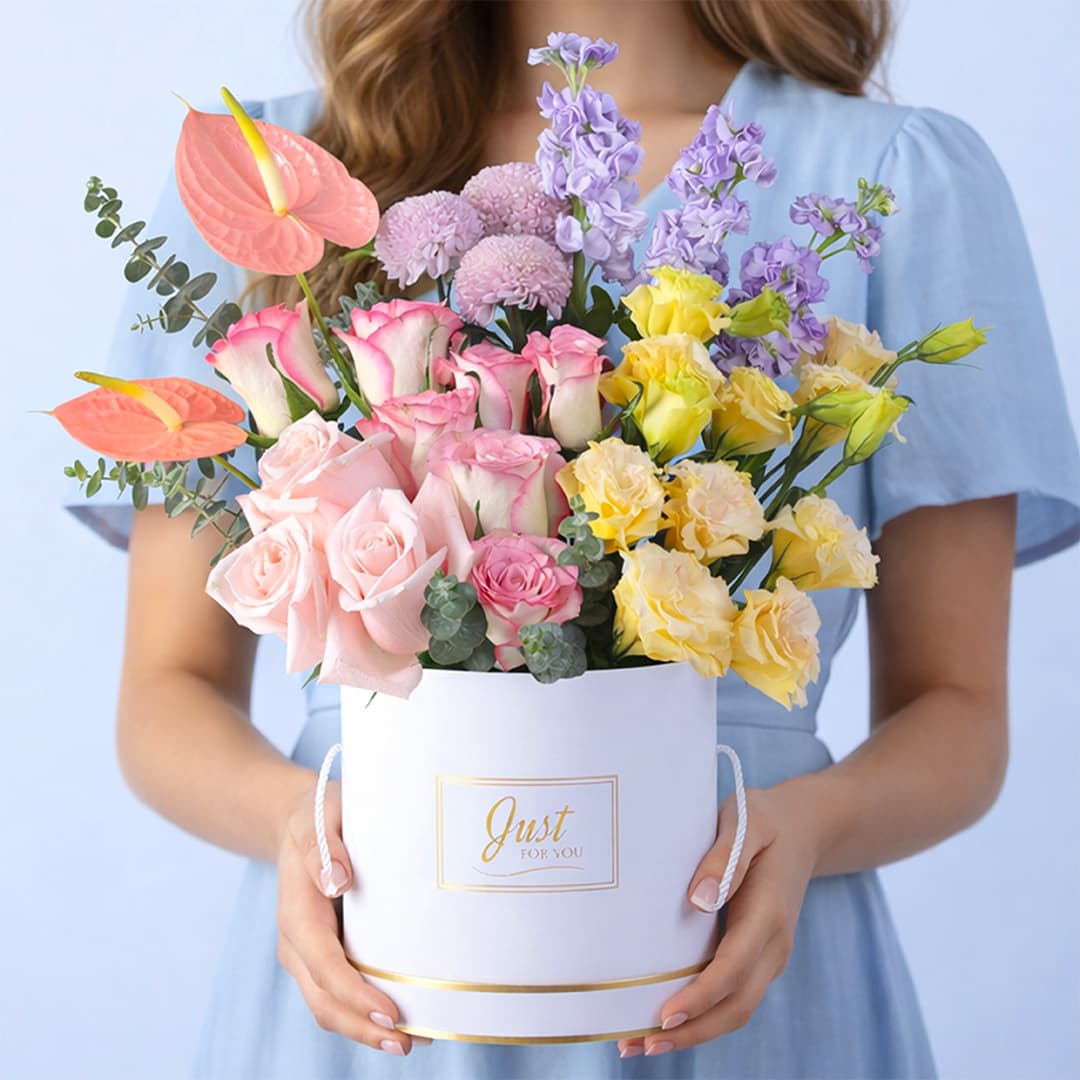 Pink roses, purple matthiola, peach anthurium, purple ping pong blooms, peach lisianthus, and eucalyptus in a white luxury round box, finished with a Just For You message label.