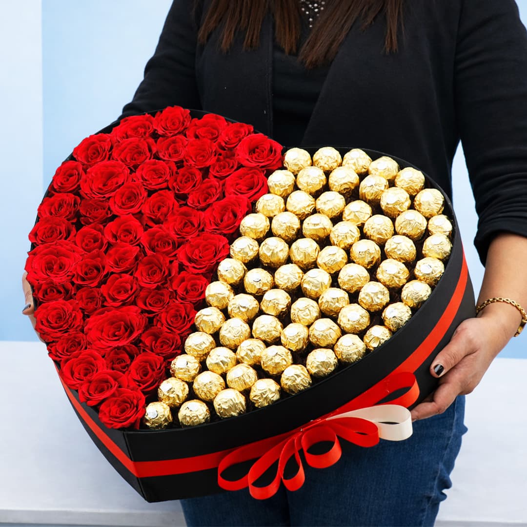 A woman holds a heart-shaped box filled with Ferrero chocolates and by 50 red roses, symbolizing love and affection.
