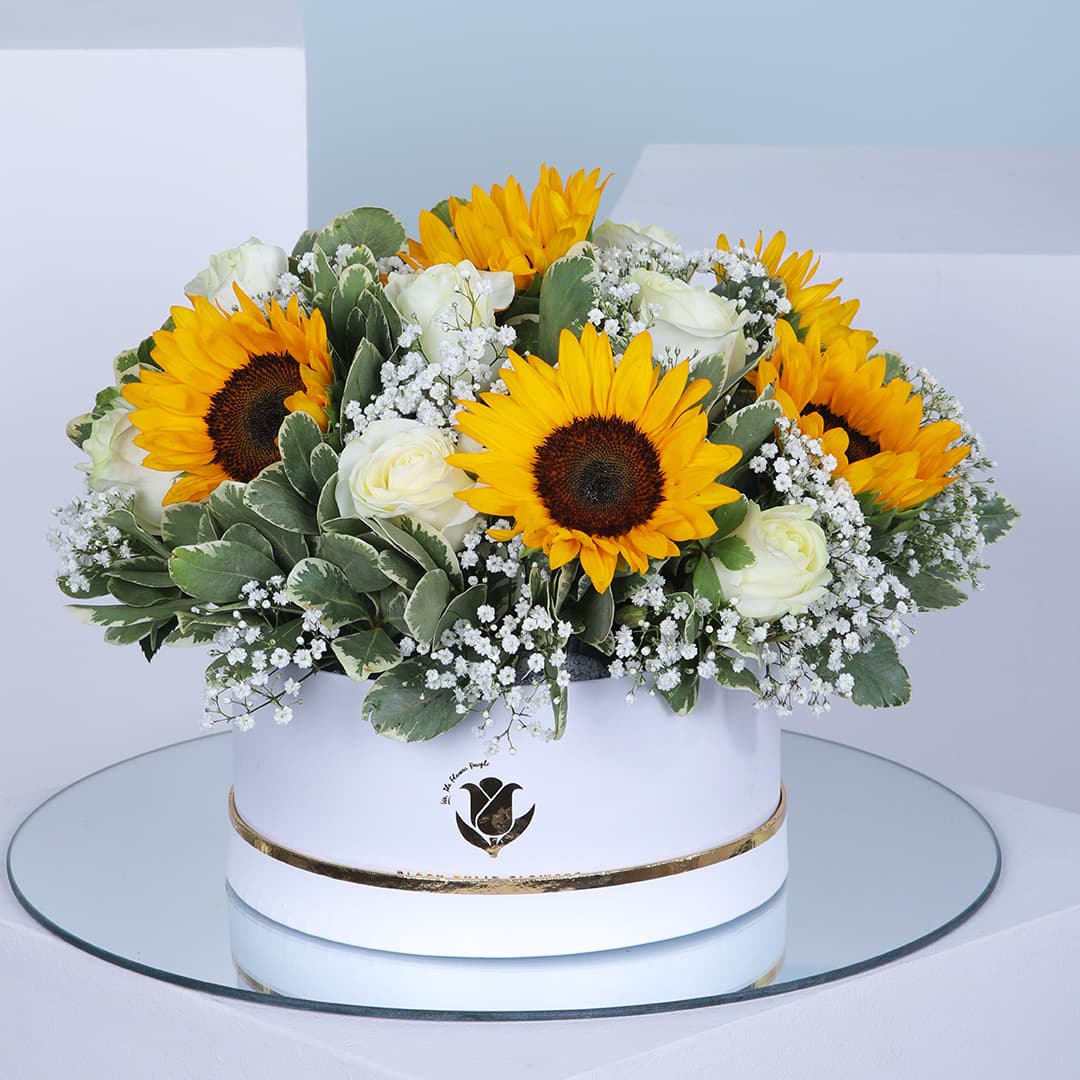 A circular box filled with a bouquet of bright yellow sunflowers and white roses.
