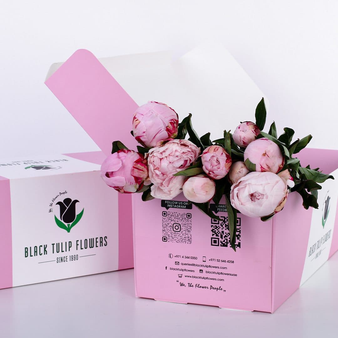 A pink box with a bouquet of pink peonies inside.