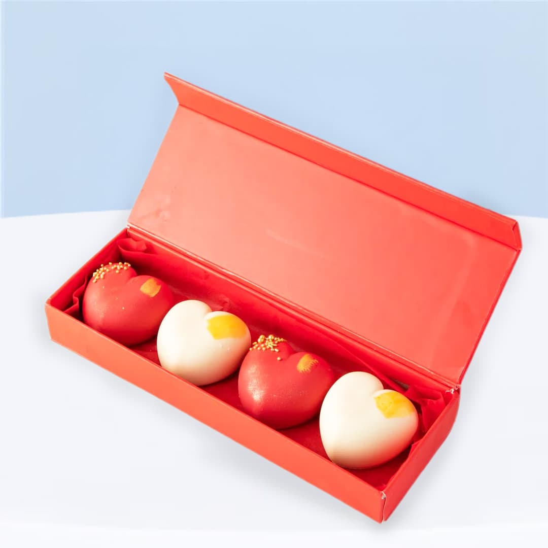 Red and white heart-shaped mini cakes in a red gift box, two red velvet and two brownie flavors.