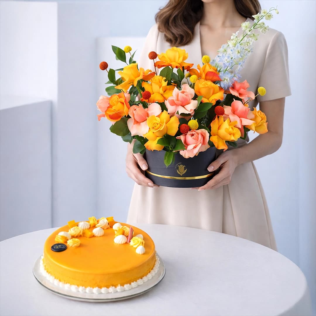 A floral arrangement box featuring fresh flowers placed beside a mango mousse cake combo.