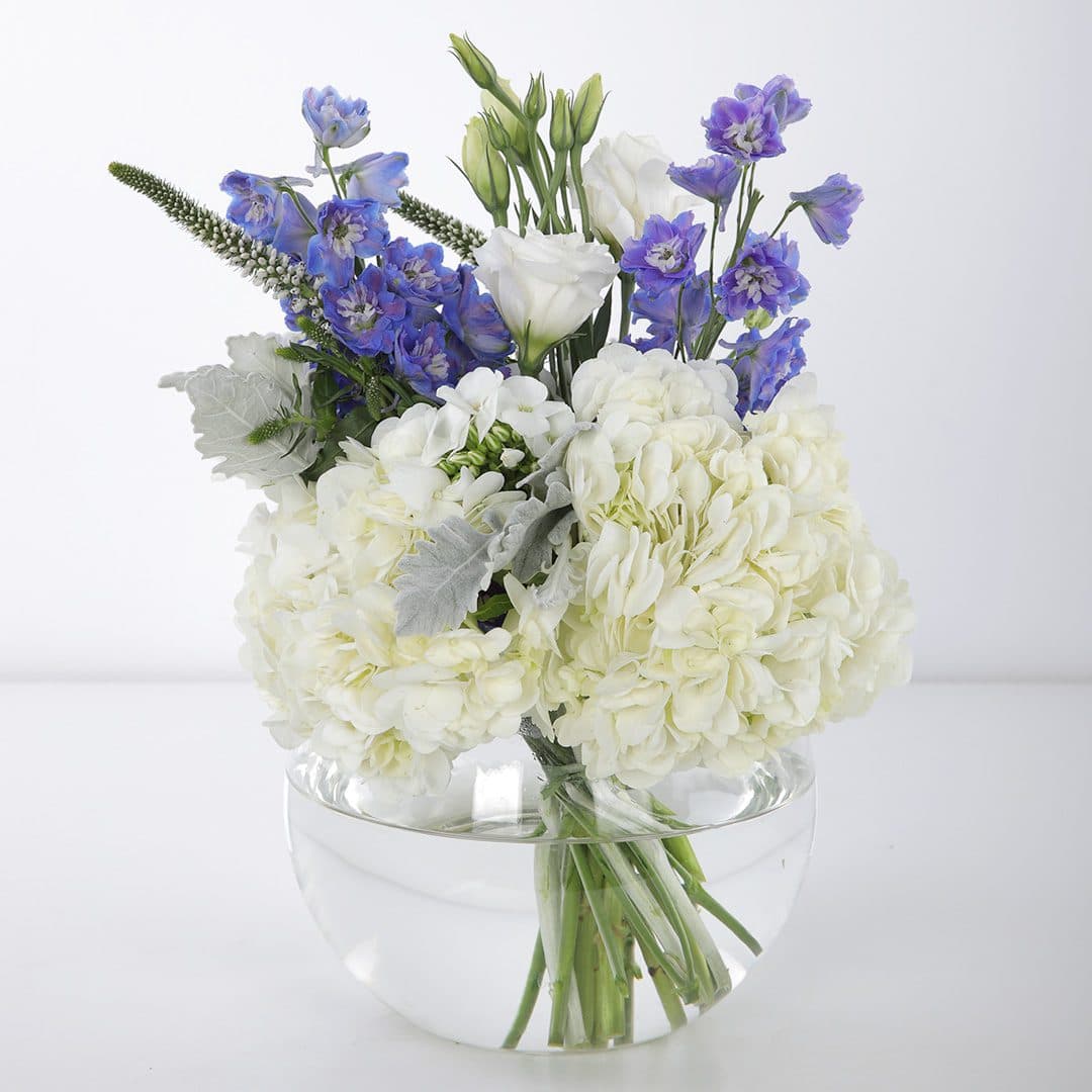 The centerpiece features blue delphinium, white hydrangeas, and other white flowers in a clear glass vase.