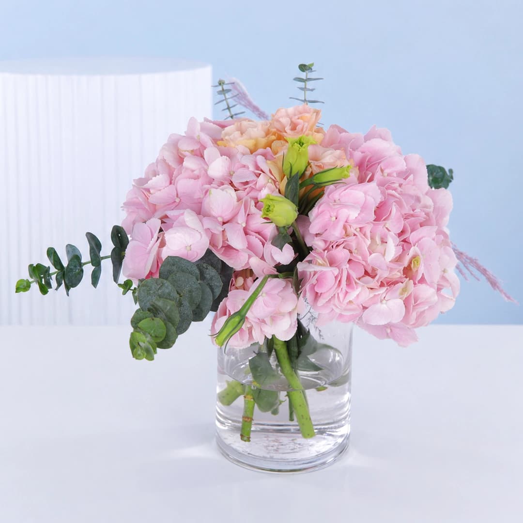 Cylindrical glass vase centerpiece featuring soft pink hydrangeas and lisianthus arranged for elegant table decor and refined event styling.
