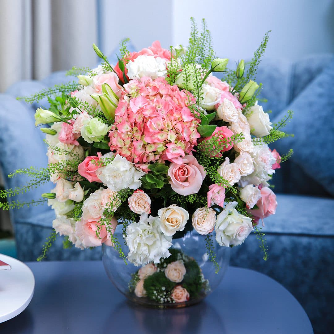 Pastel-colored assorted flowers with greenery arranged in a round glass vase.