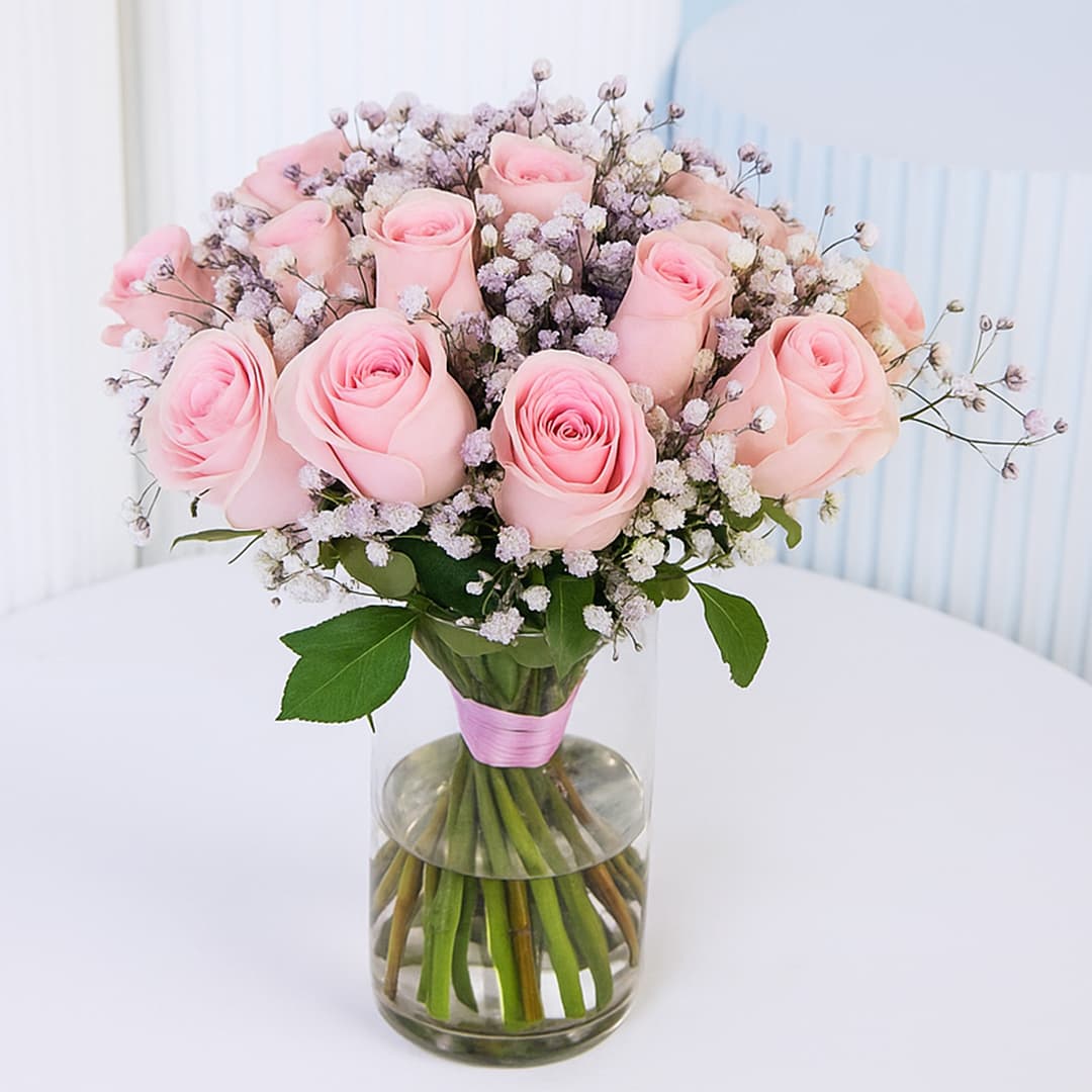 20 delicate pink roses with white baby's breath arranged in a clear glass vase with a pink ribbon.