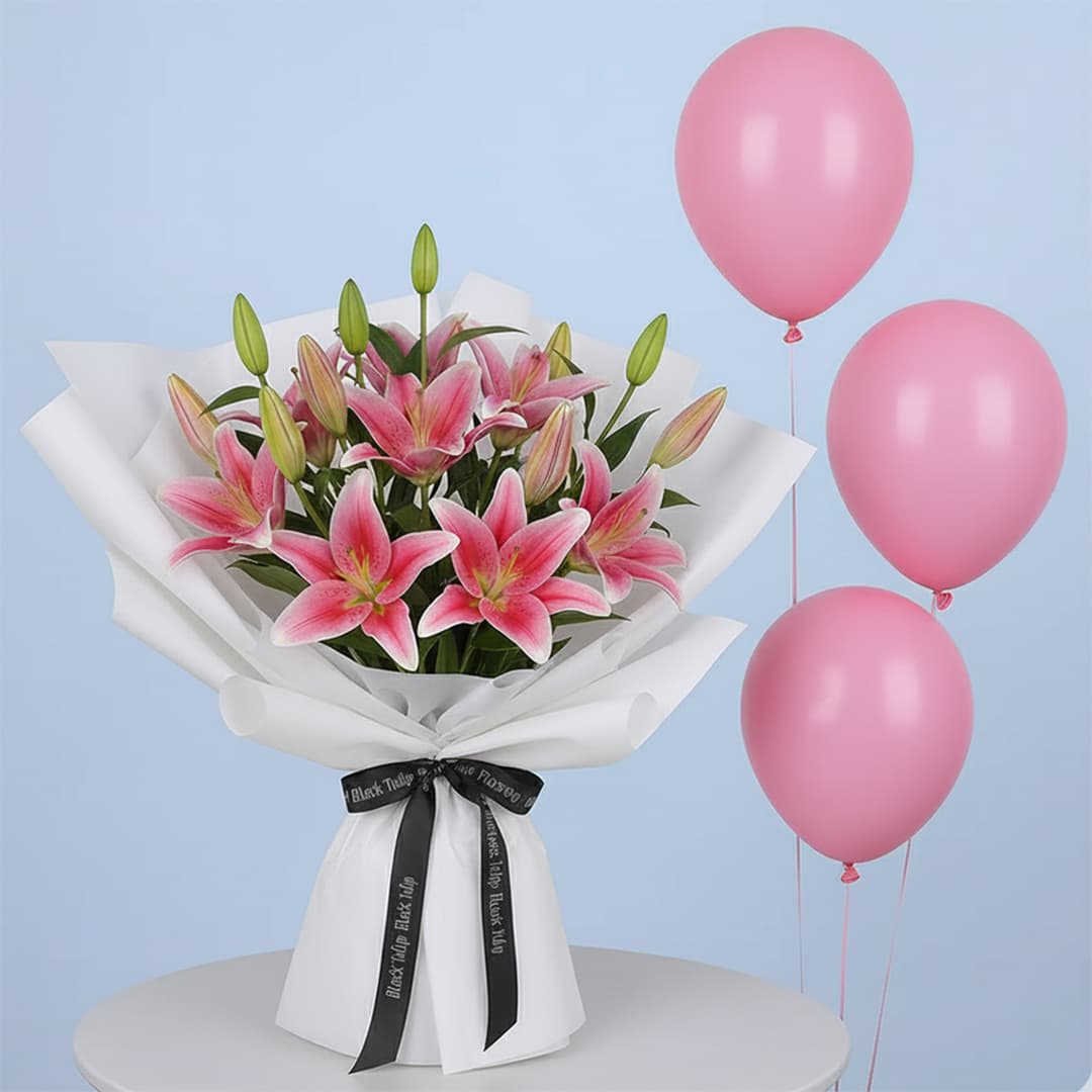 A vibrant pink lily bouquet with multiple blooming lilies and green buds, wrapped in white with a black branded ribbon and three pink balloons.