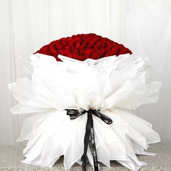 A large bouquet of 200 red roses elegantly arranged in a white wrap tied with a black ribbon.