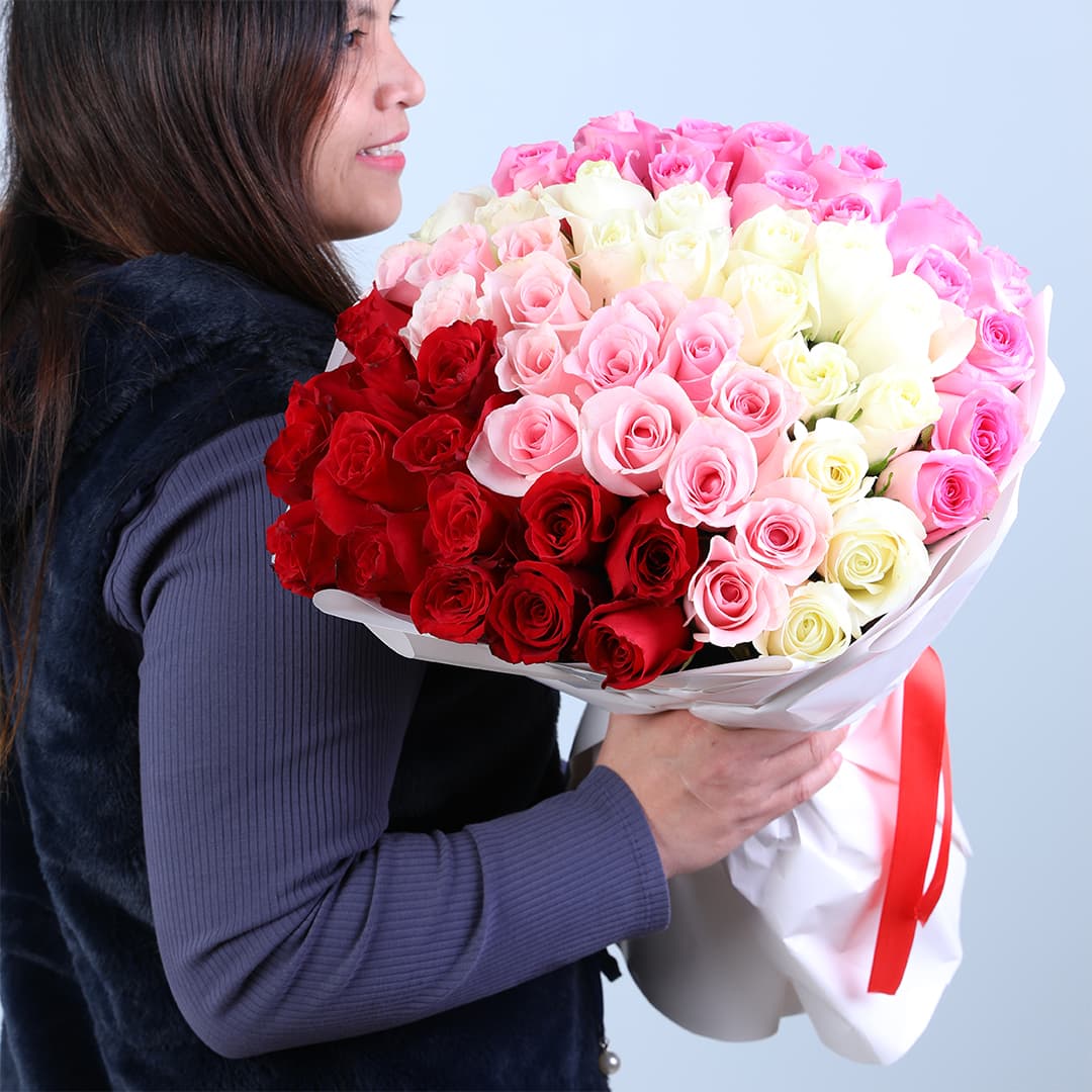 Bouquet featuring ombre red, pink and white roses in layered white wrapping with red satin ribbon.