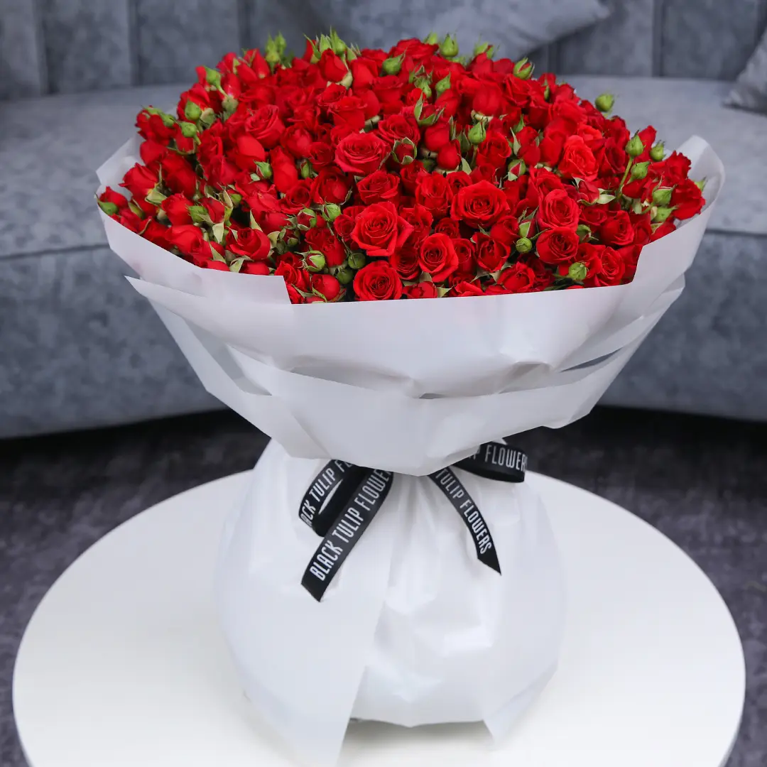 A large bouquet of red spray roses wrapped in white adorned with a black ribbon.
