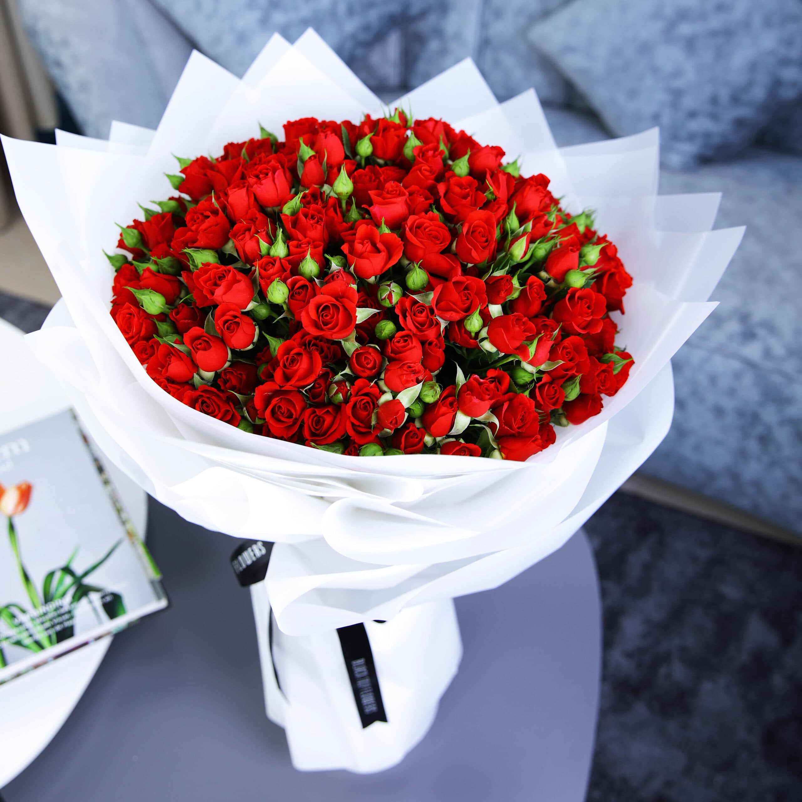 A bouquet of 50 stems of spray roses wrapped in white and tied with a black ribbon.