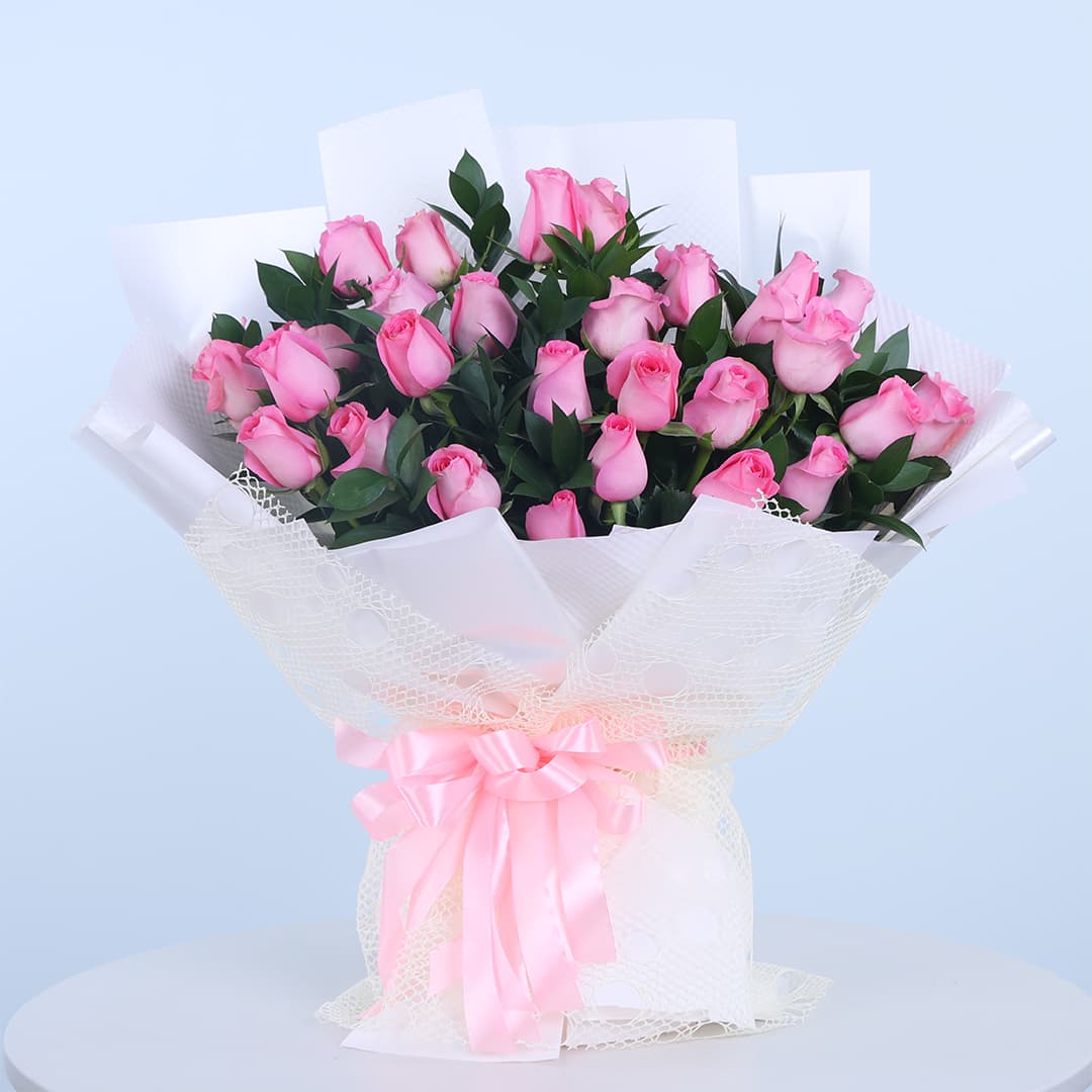 Bouquet of 30 pink roses wrapped in white with fresh green leaves.