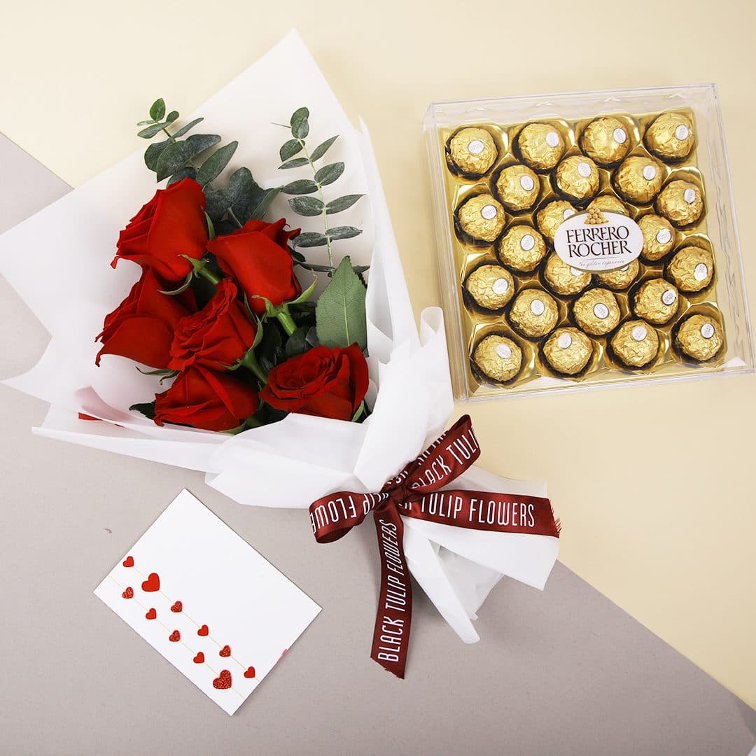 Bouquet of red roses tied with a maroon ribbon with a Ferrero box and message card.
