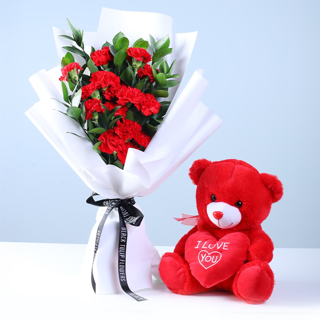 20 red carnations and ruscus bouquet, paired with a red teddy bear holding an “I Love You” message.