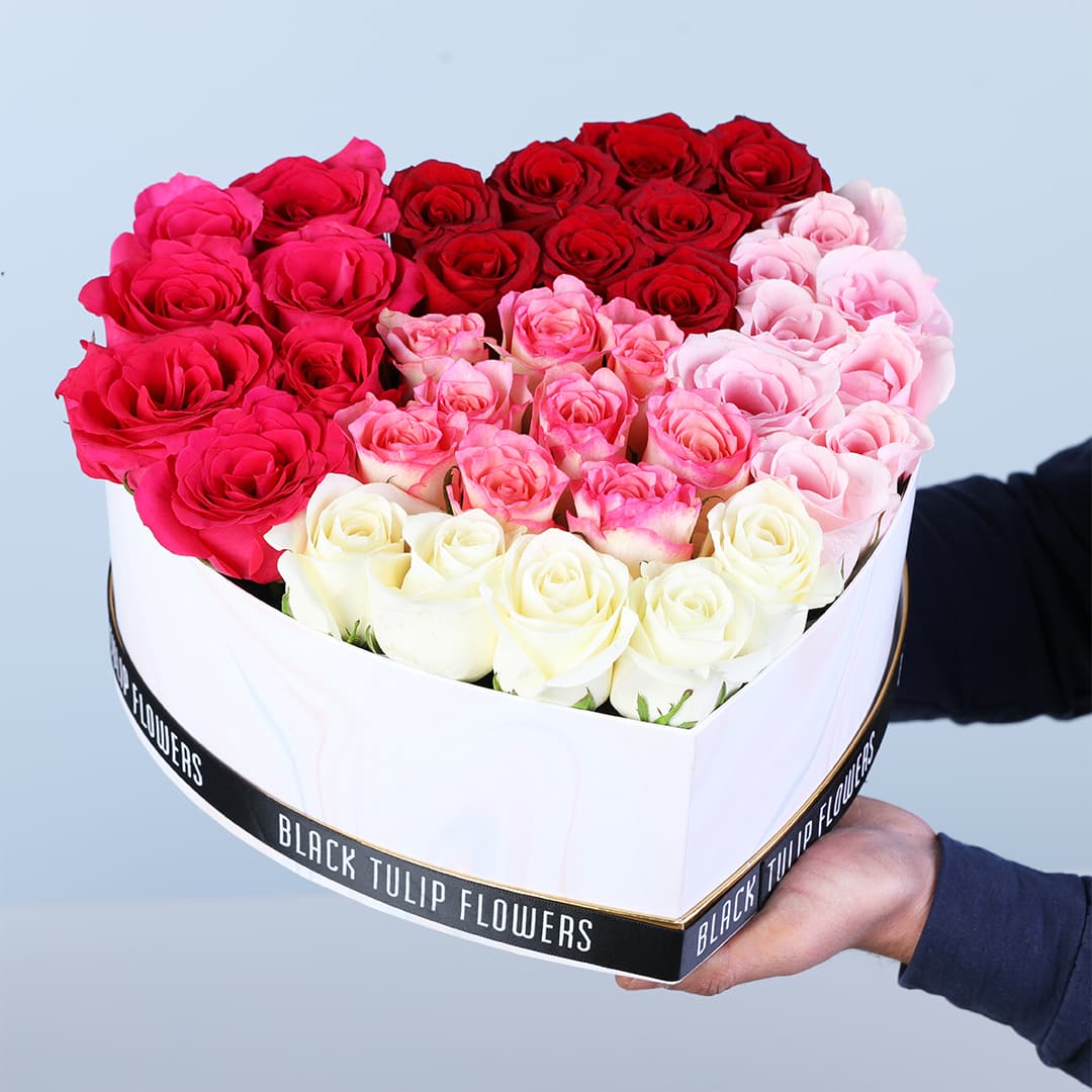 A heart-shaped box featuring red roses, pink roses and white roses.