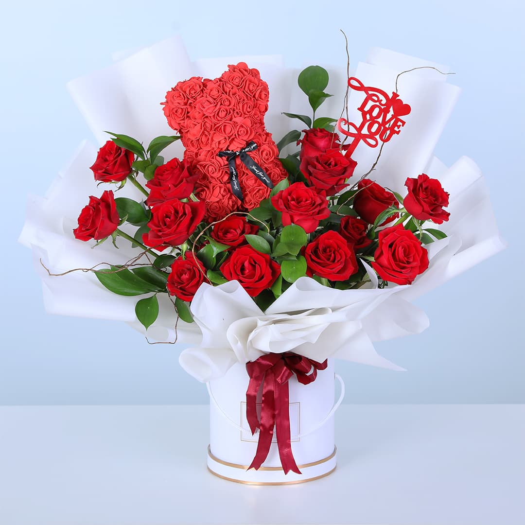 Red roses with ruscus in a white box with a rose teddy topper, finished with a “Love You” message.