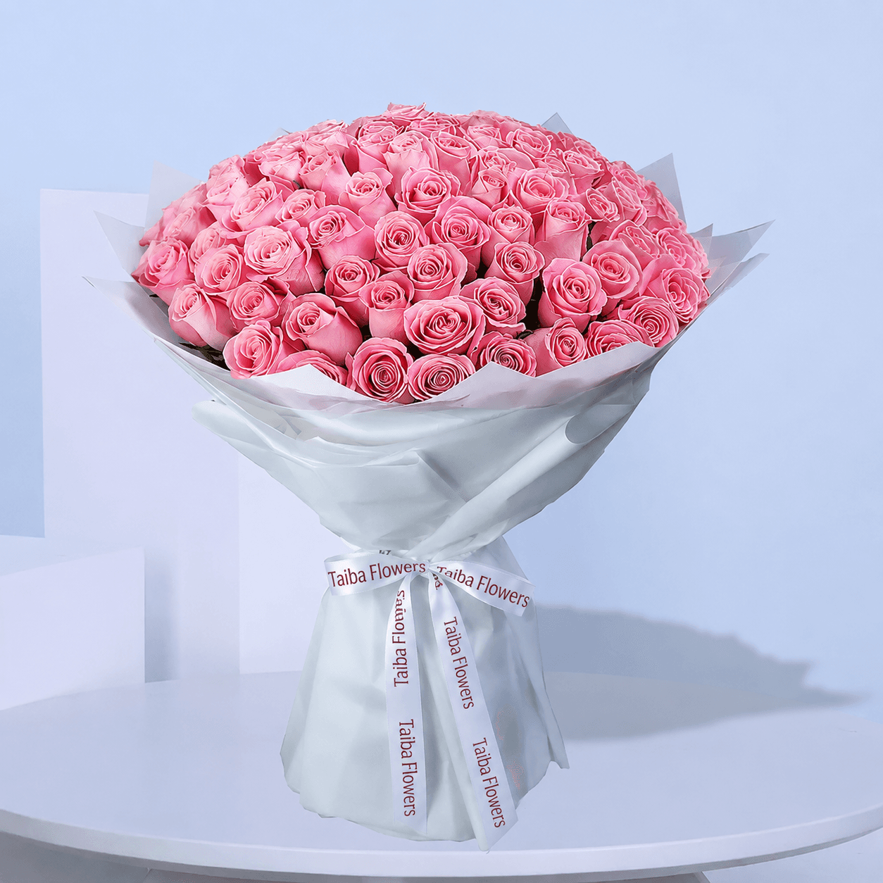 A large bouquet of light pink roses wrapped in white paper with white ribbons.
