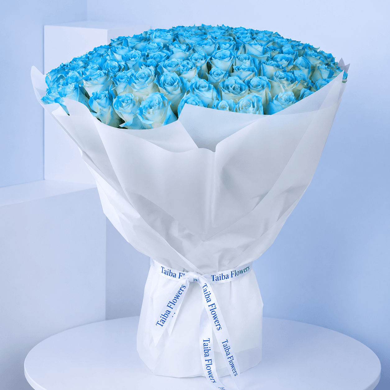 Elegant bouquet of 100 spray-painted blue roses in a white wrap tied with white ribbon.