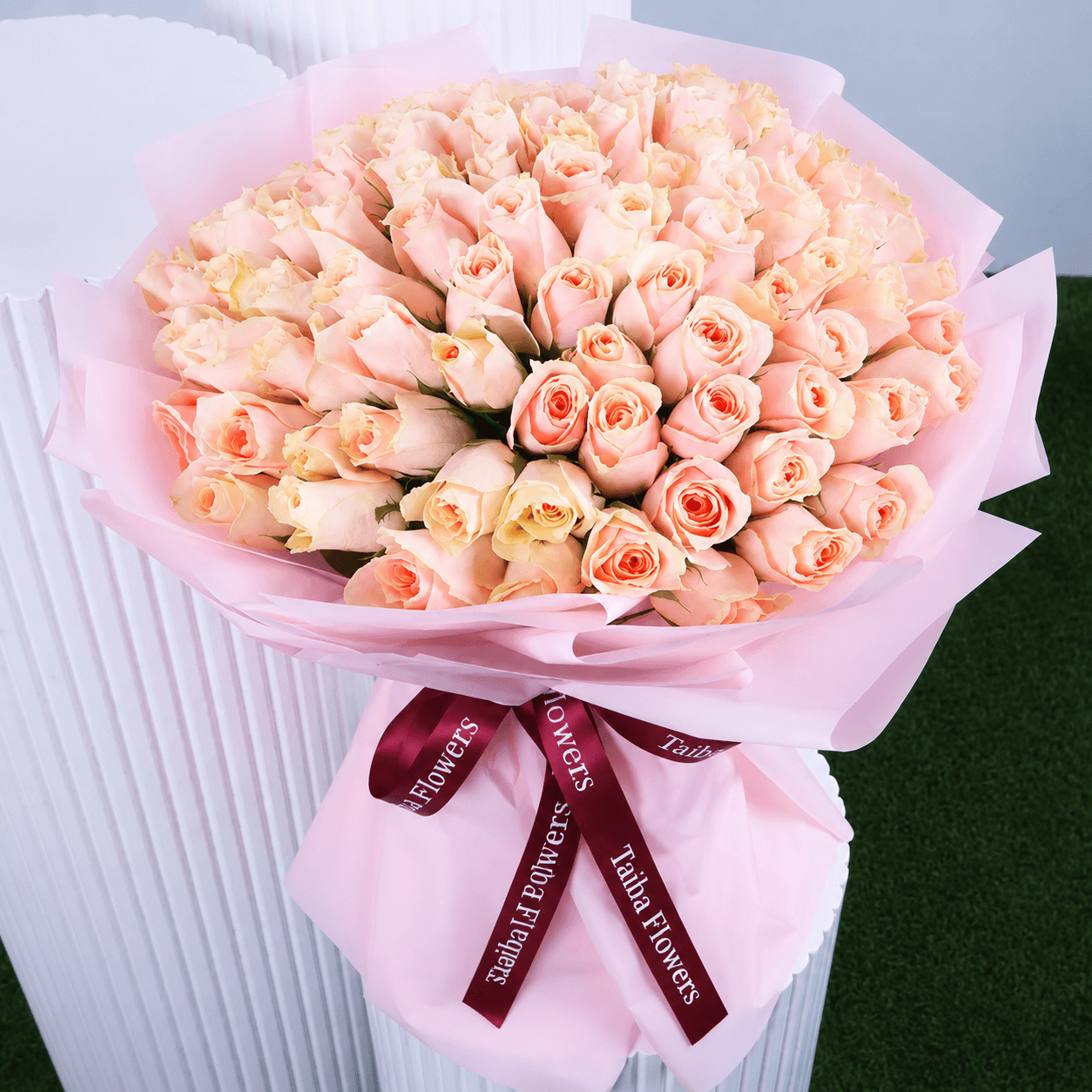 An elegant bouquet featuring fresh peach roses wrapped in blush pink paper and tied with a maroon ribbon.